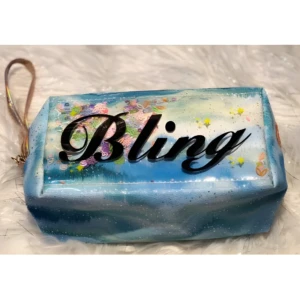 Cosmetiquera transparente con diseño floral y escarcha, texto "Bling" en negro.