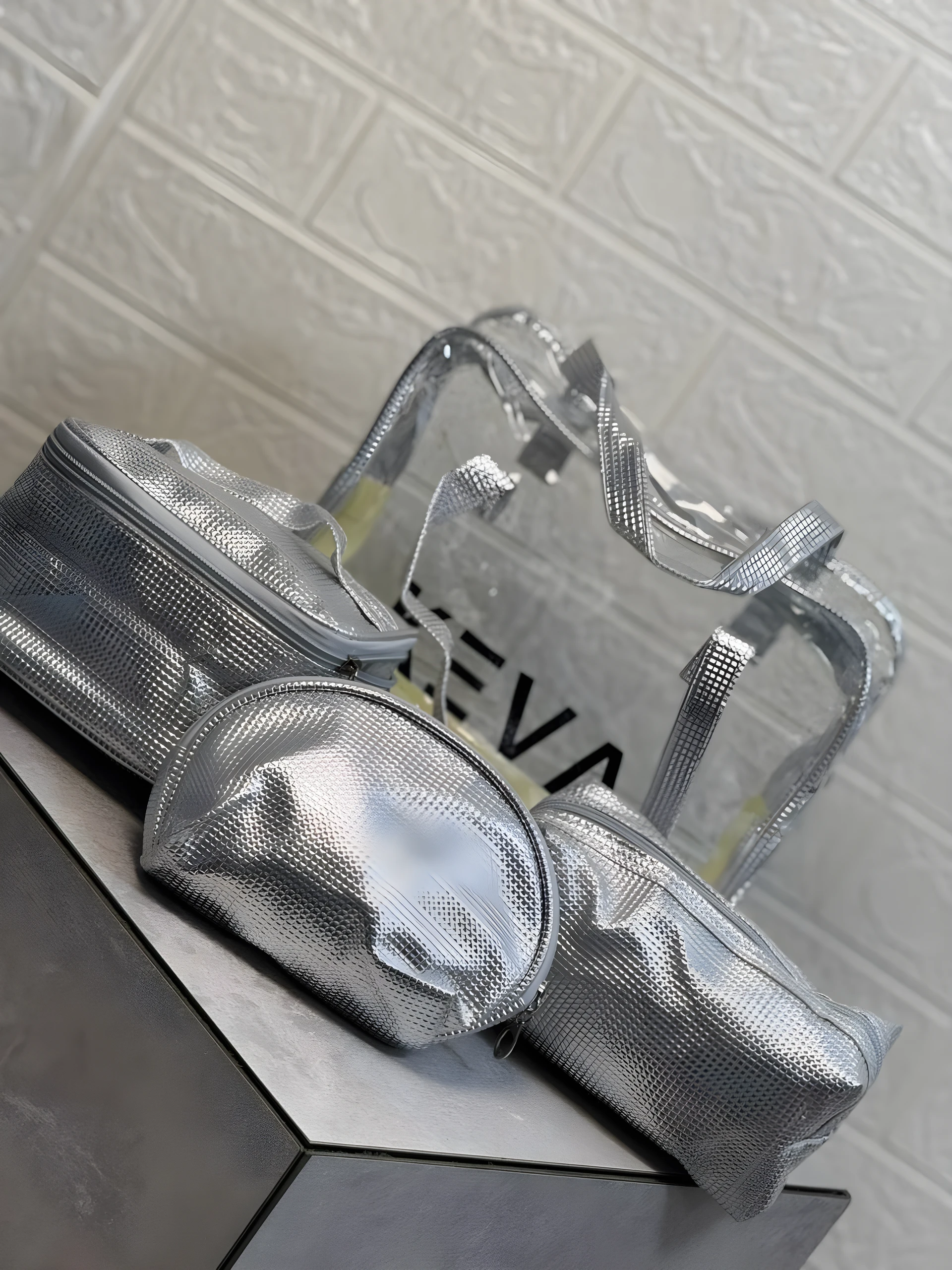 Set de 4 cosmetiqueras plateadas brillantes, textura acolchada y bolsa transparente con asas.