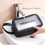 Cosmetiquera negra impermeable con texto WASHBAG en lavamanos bajo chorro de agua.