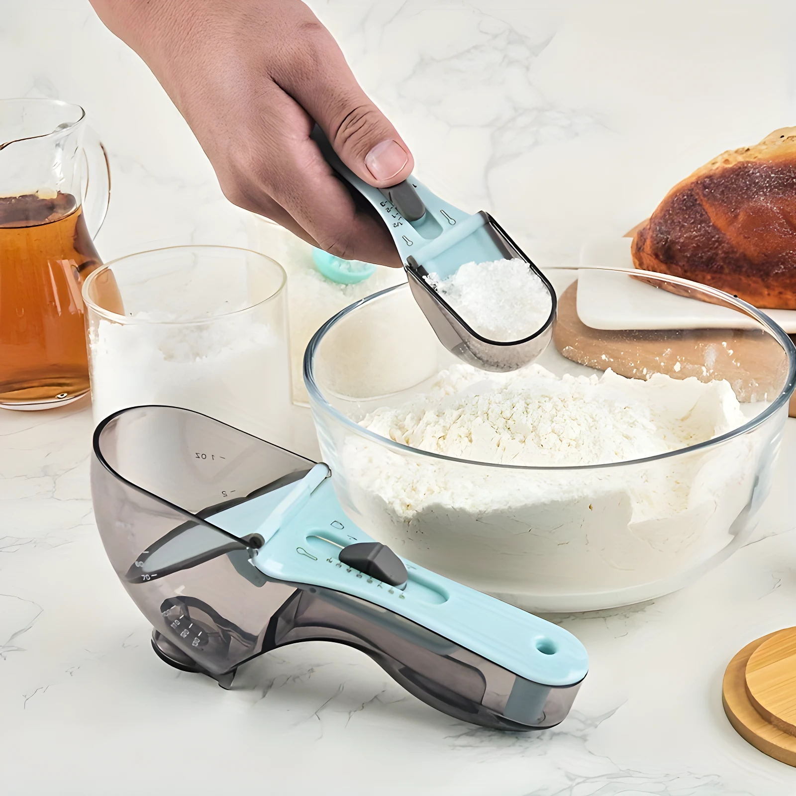 Set x2 cucharas medidoras grameras de repostería en plástico gris y azul, midiendo harina en un tazón.