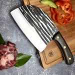 Cuchillo hachuela profesional con hoja de acero blanco texturizado, mango de madera oscura, sobre tabla de cortar de madera con pimientos y carne cruda.