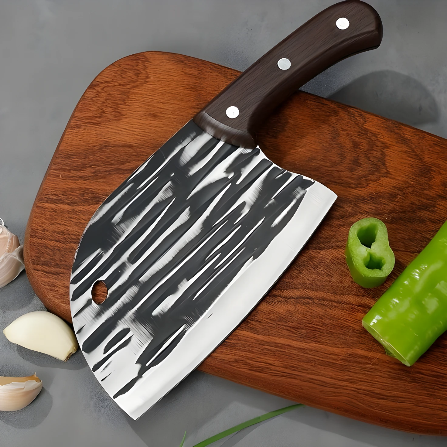 Cuchillo hachuela profesional de acero con diseño martillado y mango de madera, sobre tabla de corte con pimientos y ajos.