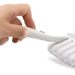Depilador facial eléctrico blanco "Flawless" con luz LED, sostenido por mano, ideal para cejas y piel lisa.