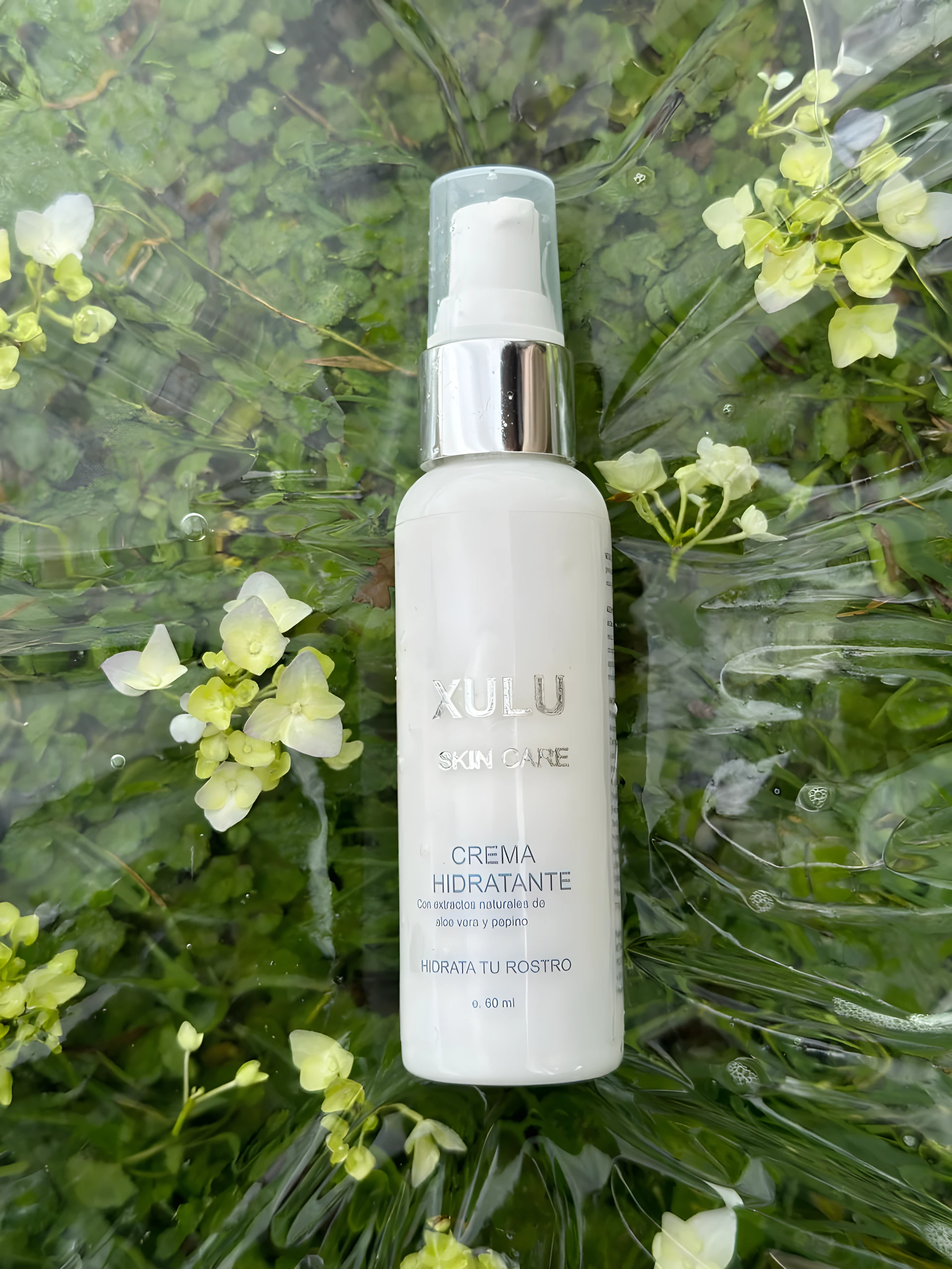 Crema hidratante Xulu Skin Care en envase blanco con detalles plateados, sobre fondo verde y flores, 60 ml.