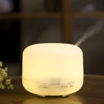 Difusor de aromas ultrasónico blanco 500 ml con vapor suave, emite luz cálida y cuenta con botones de control para luz y temporizador.