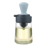 Dispensador de aceite con brocha integrada, cuerpo de vidrio y tapa gris con brocha azul claro para cocinar.