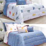 Edredón infantil doble faz con dinosaurios, azul y blanco, con cojines decorativos.