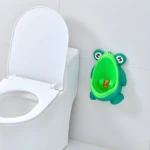 Orinal infantil con forma de sapito verde, con hélices naranjas, al lado de un inodoro blanco en un baño.