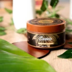 Exfoliante corporal Cocoa en tarro marrón, 220 ml, con hojas verdes sobre mesa de madera.