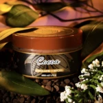 Exfoliante corporal Cocoa de 220 ml en frasco naranja, rodeado de granos de chocolate y hojas verdes.