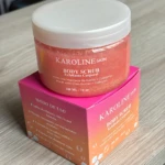 Exfoliante corporal Karoline Skin, rosado con brillos, en envase transparente sobre caja rosada. 300ml.
