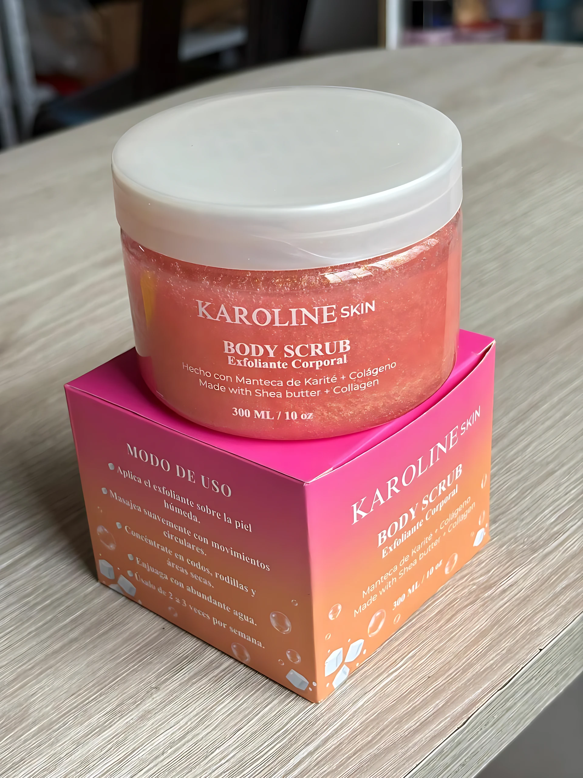 Exfoliante corporal Karoline Skin, rosado con brillos, en envase transparente sobre caja rosada. 300ml.