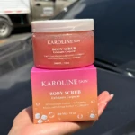 Exfoliante corporal Karoline Skin 300 ML, fragancia a rosas, en envase rosa y su caja, sostenido por una mano.