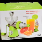 Extractor de jugos manual verde con manivela, vaso de jugo, frutas y helado, empaque de nutrición.