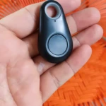 Extractor de jugos manual negro con localizador Bluetooth en mano, fondo naranja.