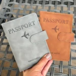Dos fundas de pasaporte, una gris y otra naranja, con diseño de avión y texto "travel wallet".