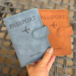 Set x2 fundas de viaje para documentos, color azul y naranja, con avión grabado, sostenidas por mano.