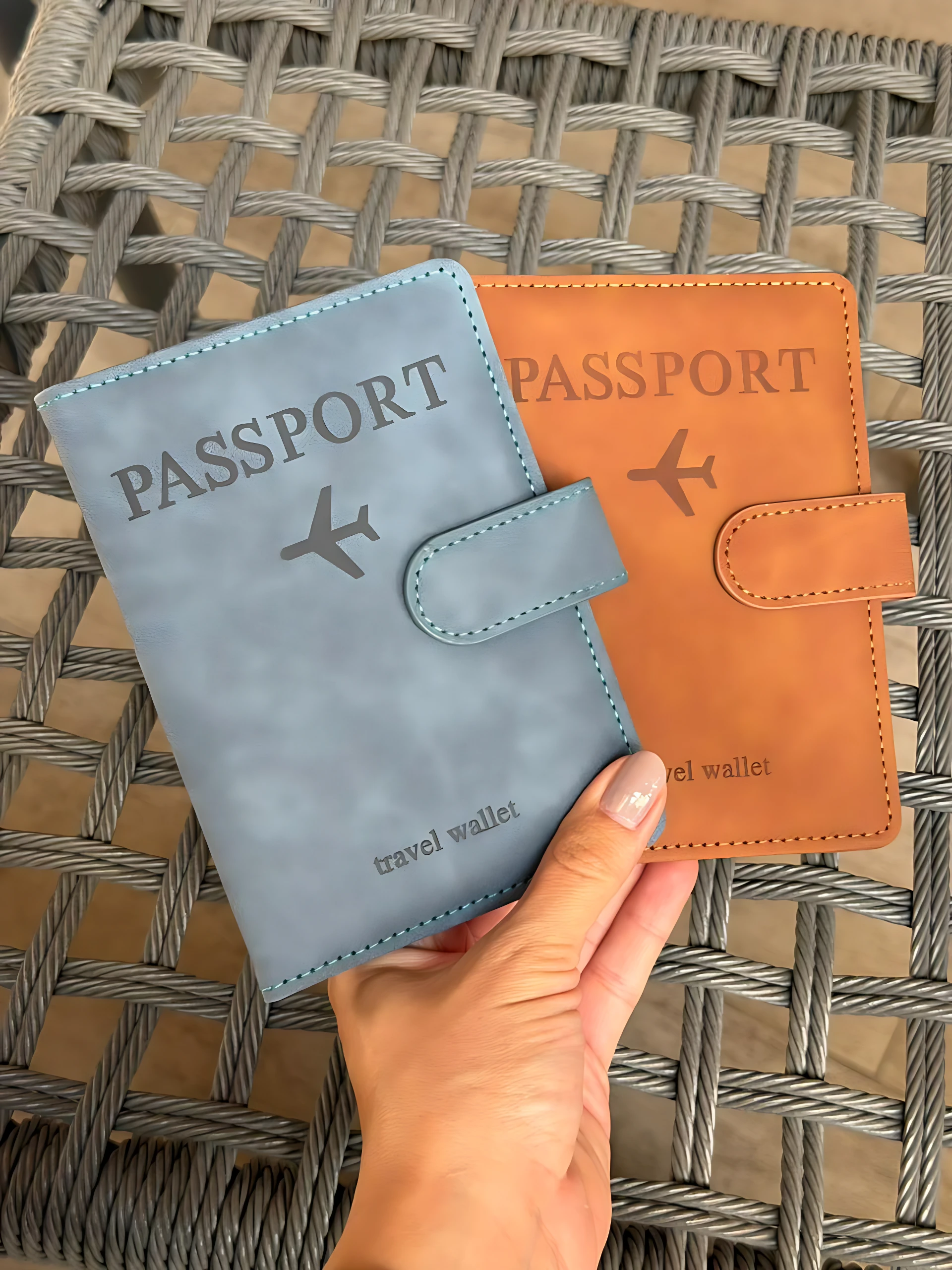 Set x2 fundas de viaje para documentos, color azul y naranja, con avión grabado, sostenidas por mano.