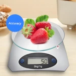 Balanza de cocina digital plateada con base de vidrio, 5kg/1g, mostrando 50g con fresas y pan en el fondo.