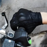 Guantes de moto negros de cuero perforado, con protecciones en nudillos, para agarre y control.