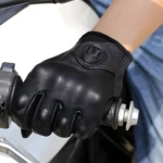 Guantes de moto negros en cuero, con cierre ajustable, sobre manillar con agarre.