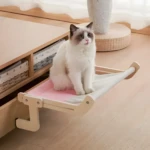 Hamaca para gato de tela color rosa y gris claro, con estructura de madera clara, sobre un sofá.