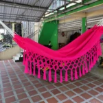 Hamaca colgante rosa vibrante con flecos, ideal para relajar niños, sobre suelo de baldosa roja.