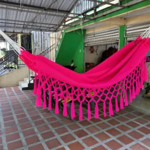 Hamaca colgante rosa vibrante con flecos, ideal para relajar niños, sobre suelo de baldosa roja.