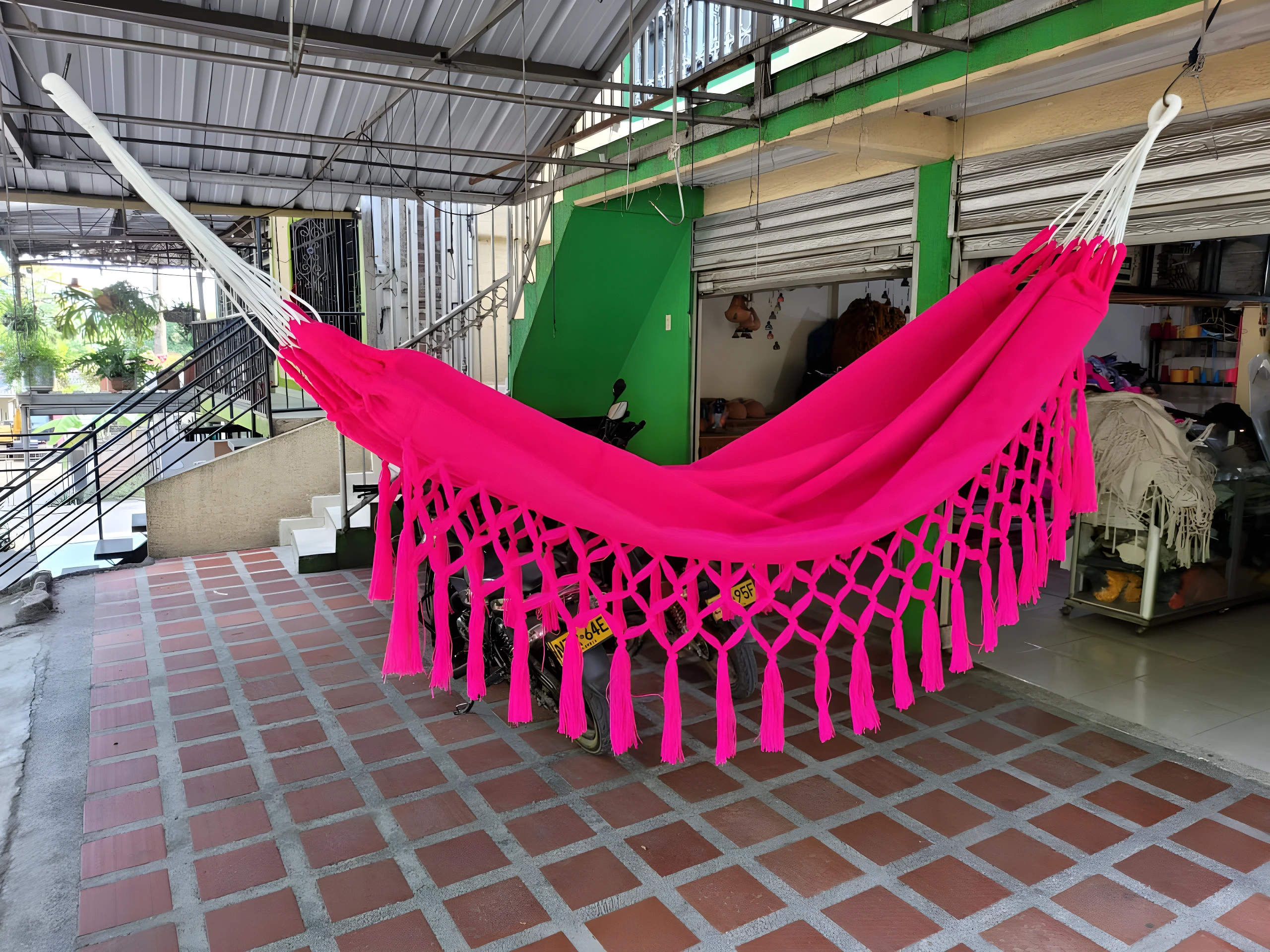 Hamaca colgante rosa vibrante con flecos, ideal para relajar niños, sobre suelo de baldosa roja.