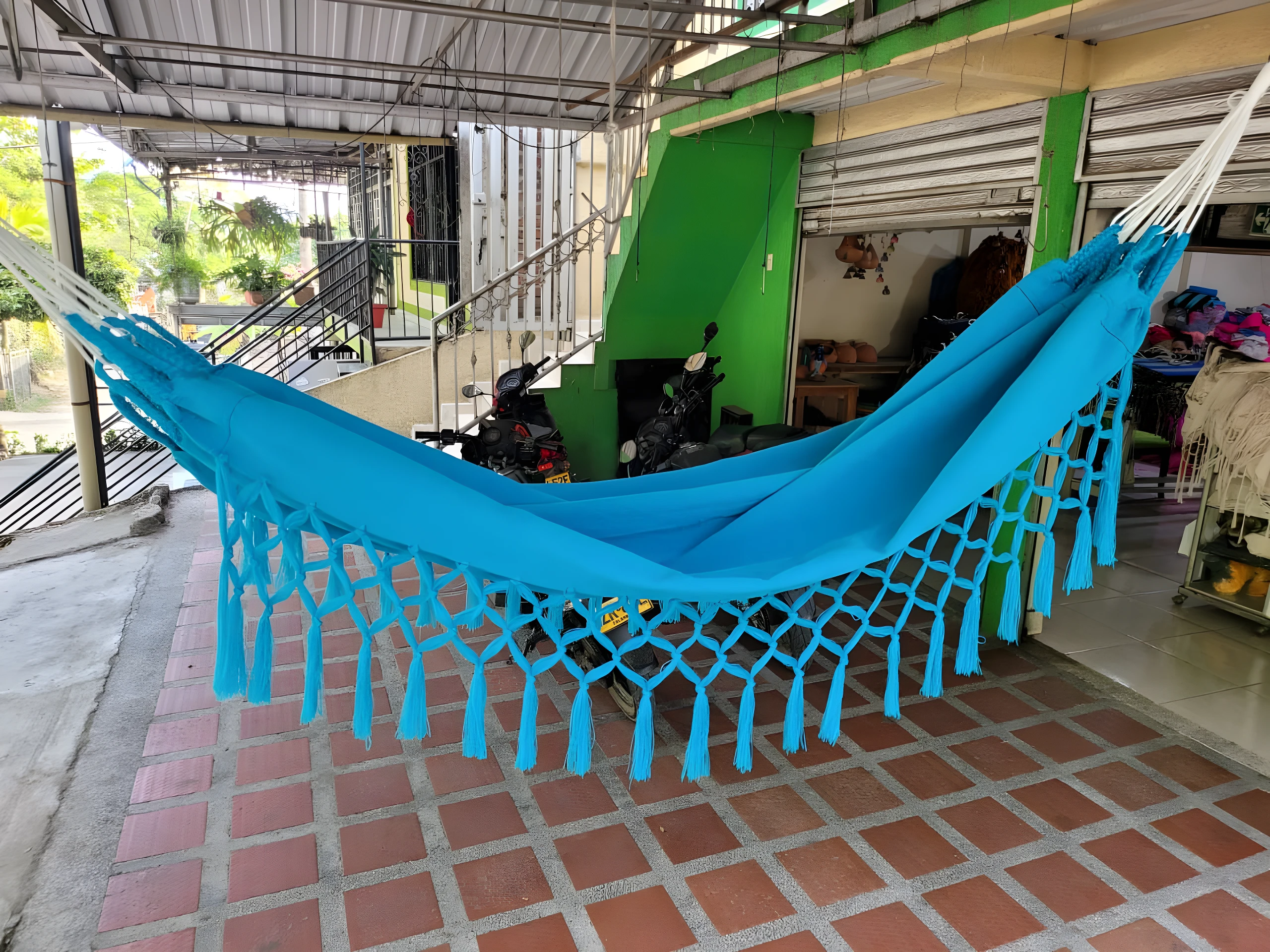 Hamaca colgante azul con flecos, ideal para relajar niños, vista exterior con terraza y escaleras.