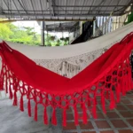 Hamaca infantil roja y blanca con flecos, ideal para relajación segura al aire libre.