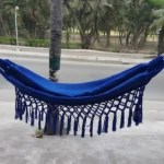 Hamaca colgante azul vibrante con flecos, atada a árbol, ideal para relajar niños.