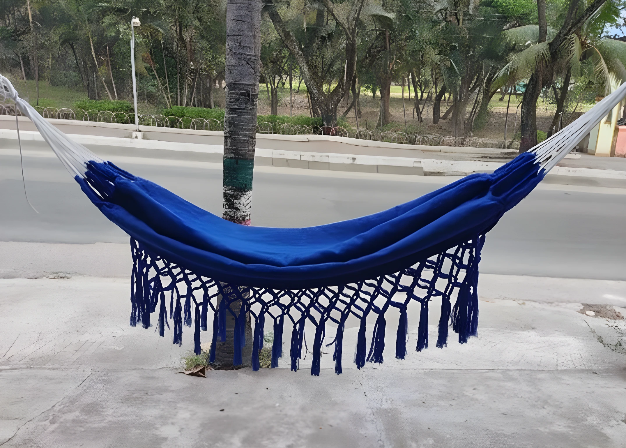 Hamaca colgante azul vibrante con flecos, atada a árbol, ideal para relajar niños.