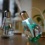 Humidificador difusor con forma de bombilla, agua azul, luz LED, palmeras decorativas y vapor.