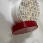 Envase blanco de inositol en polvo con tapa roja retirada, mostrando un sello de seguridad protector sobre la boca del frasco sobre fondo blanco.