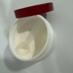 Tarro de inositol en polvo con tapa roja abierta, incluye una cuchara medidora de plástico transparente en su interior sobre el suplemento blanco.