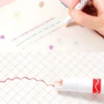 Rotuladores de curva color rojo y morado dibujando líneas decorativas en cuaderno cuadriculado y blanco.