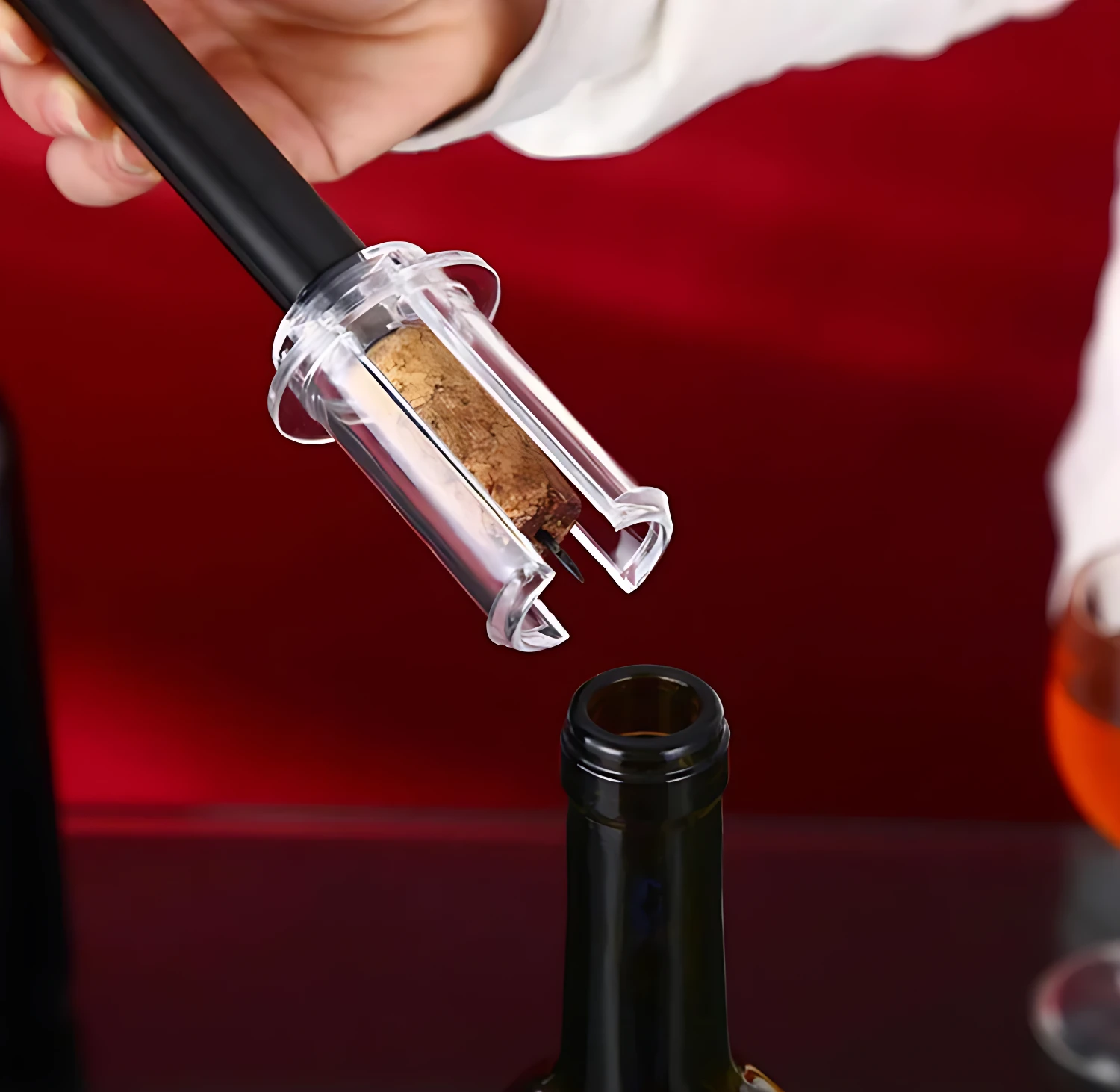 Sacacorchos de aire a presión sacando corcho de botella de vino, con cortador de cápsula y copa a un lado.