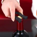 Sacacorchos de presión de aire negro abriendo botella de vino tinto con cortador de cápsula.