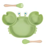 Vajilla adherente verde en forma de cangrejo con tenedor y cuchara de madera para bebés.