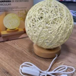 Lámpara de escritorio circular de mimbre beige con base de madera y cable USB.