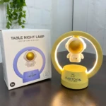 Lámpara LED de mesa con astronauta flotante, una en empaque y otra en base amarilla brillante.