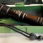 Linterna LED negra 2500 lúmenes potente en estuche verde, con correa y carga de emergencia.