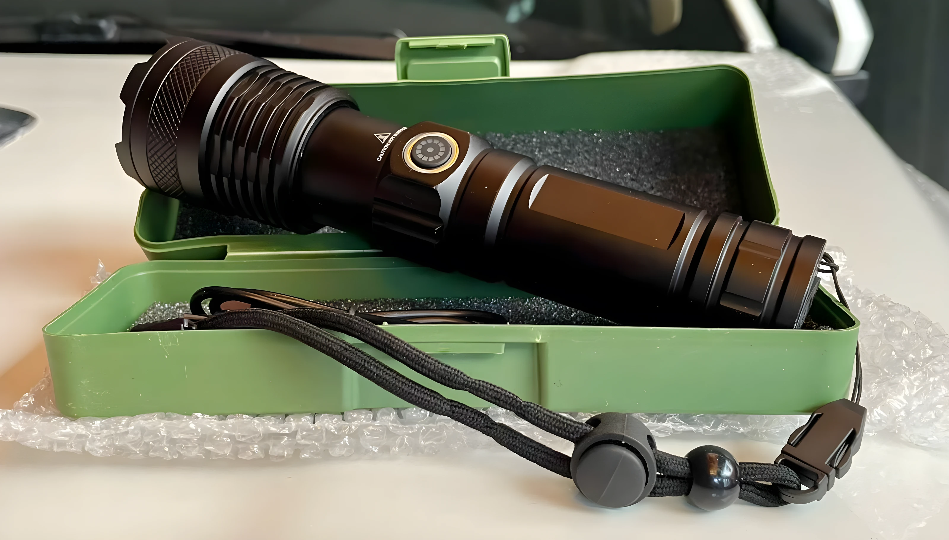 Linterna LED negra 2500 lúmenes potente en estuche verde, con correa y carga de emergencia.