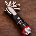 Linterna LED multiusos plateada y negra con múltiples herramientas desplegadas, sobre madera.