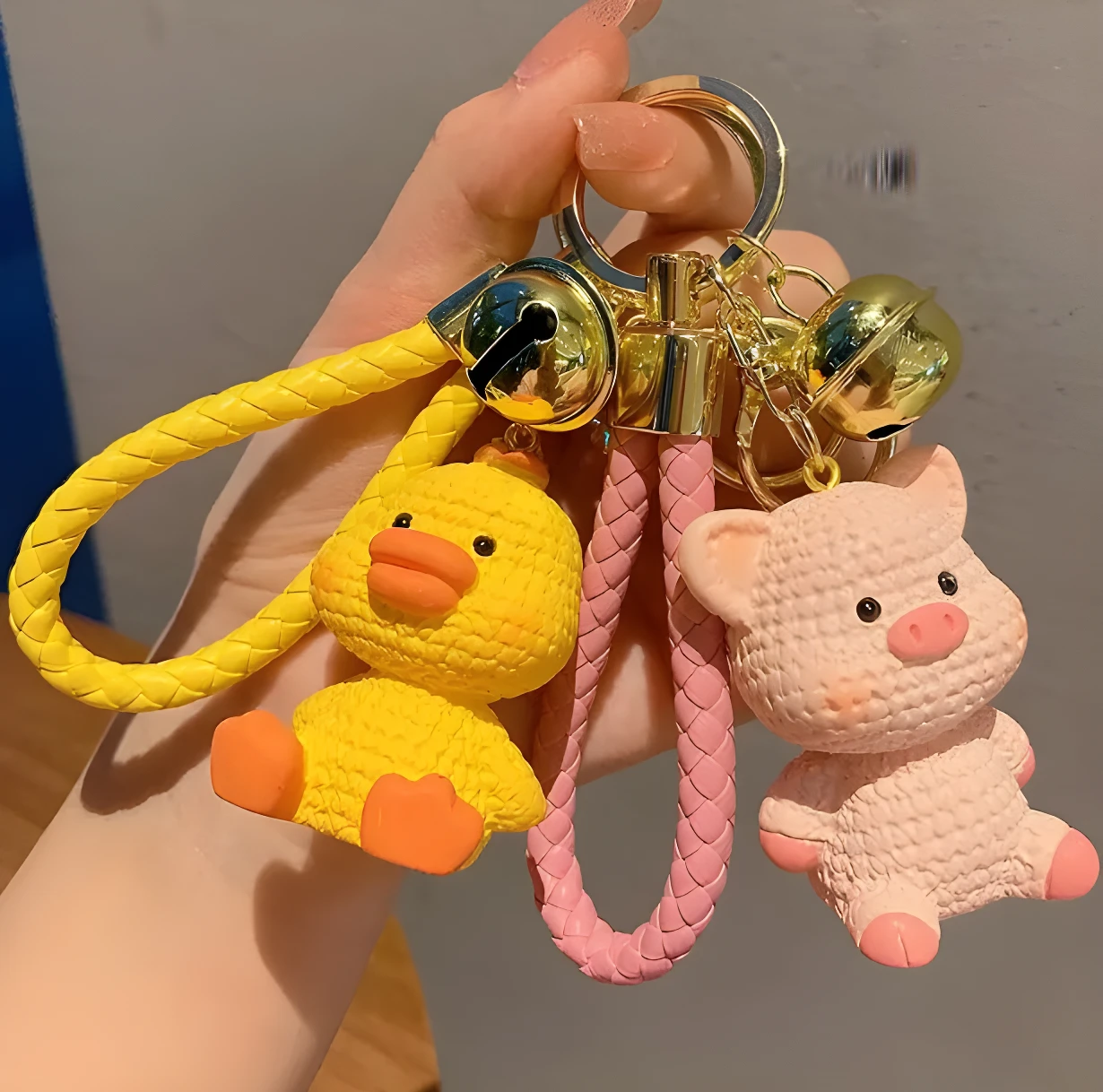 Llavero colgante bolso escolar con figura de pato amarillo y cerdito rosa, material texturizado, con cascabeles dorados.