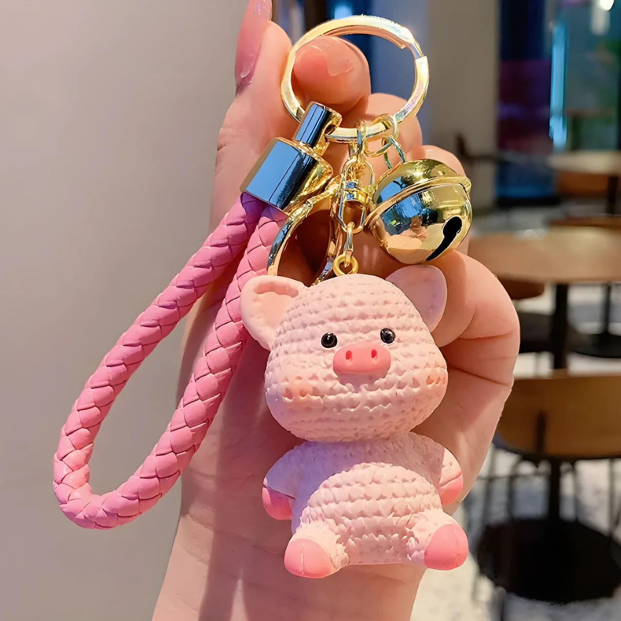 Llavero colgante de bolso escolar con forma de cerdito rosa texturizado, campanita dorada y correa trenzada.