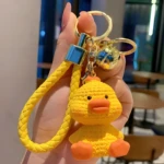Llavero de pato amarillo sentado, con correa trenzada y cascabel.