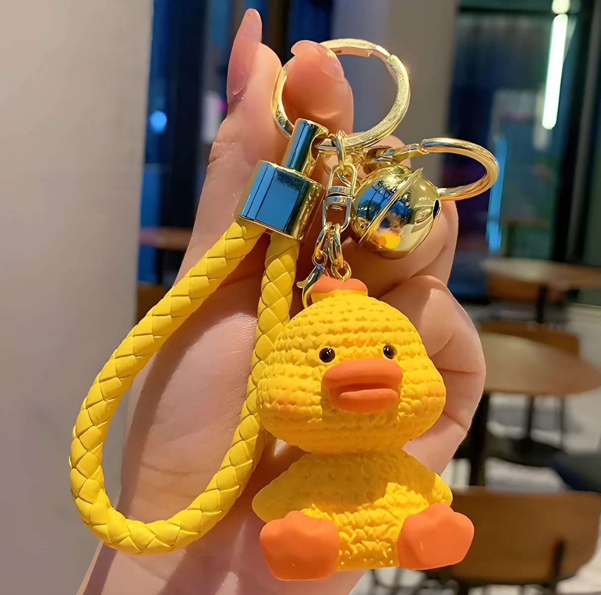 Llavero de pato amarillo sentado, con correa trenzada y cascabel.