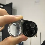 Lupa joyero plegable de metal con múltiples lentes y tornillos visibles, sostenida por mano.